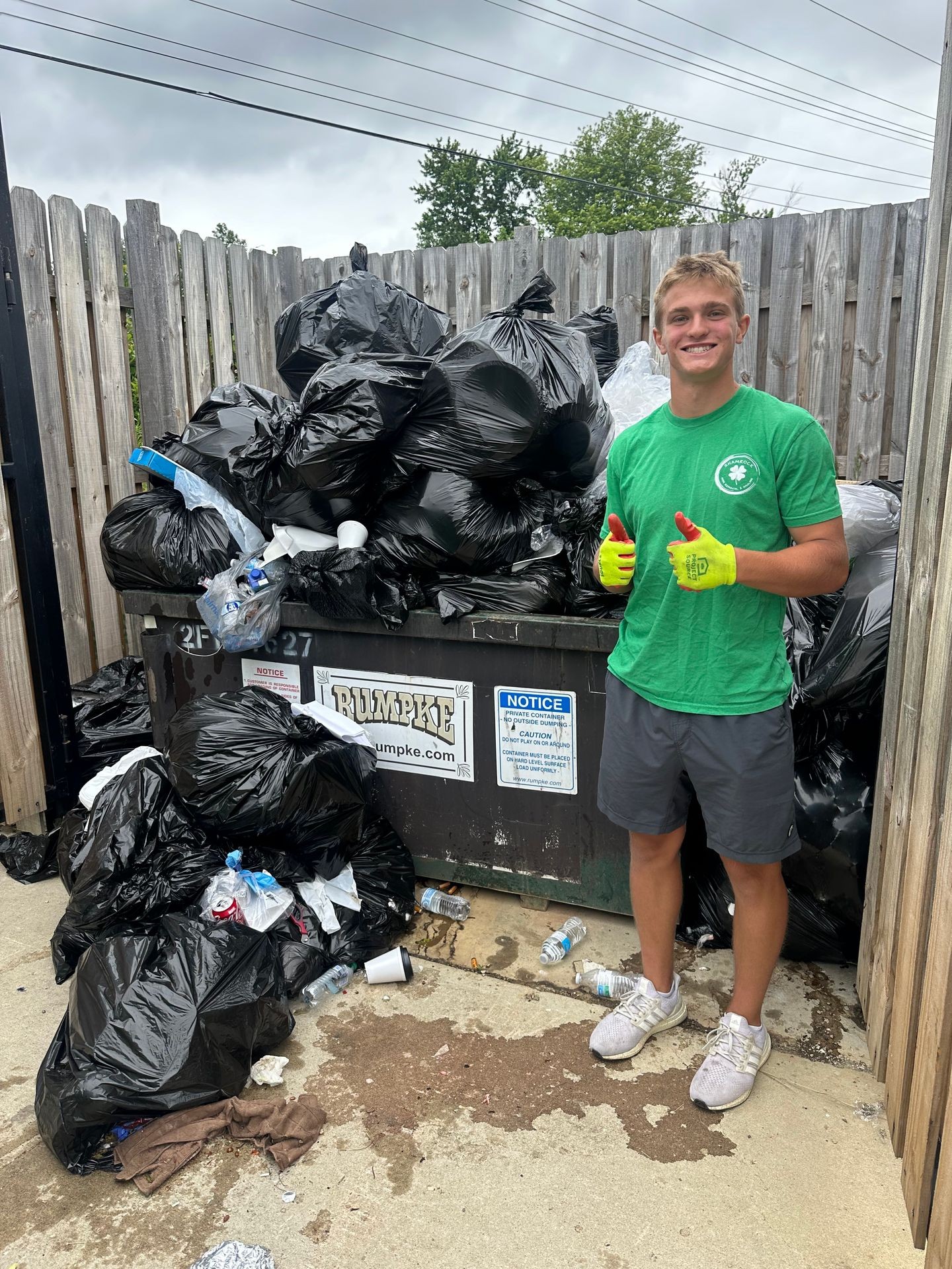 Shamrock Junk Removal and Hauling Owner Garrett Peterson Stands in front of a overflowing dumpster