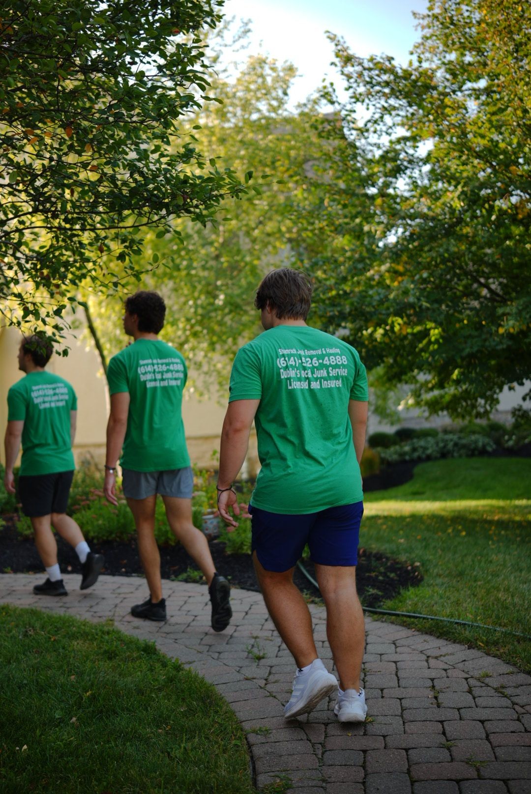 Three Shamrock Junk Removal employees walking on a brick path while completing a moving job in Muirfield