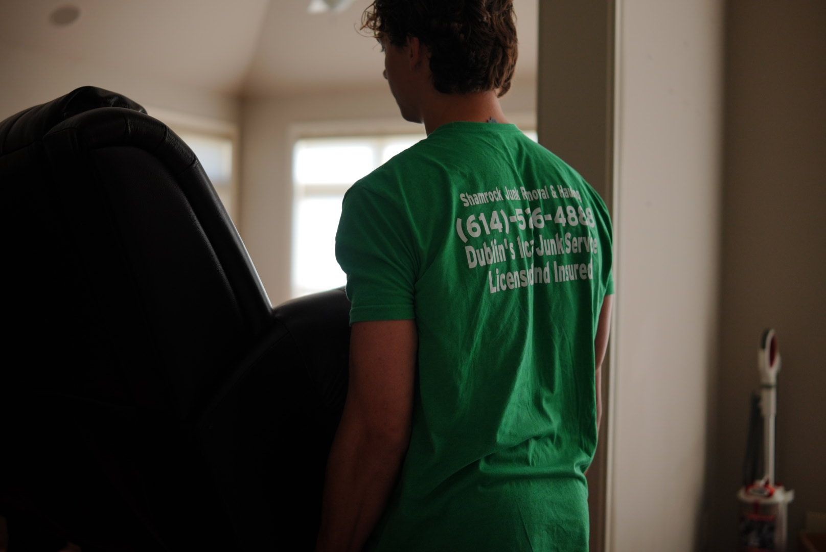 Shamrock Junk Removal moves furniture inside a room with a vacuum cleaner visible in the background.