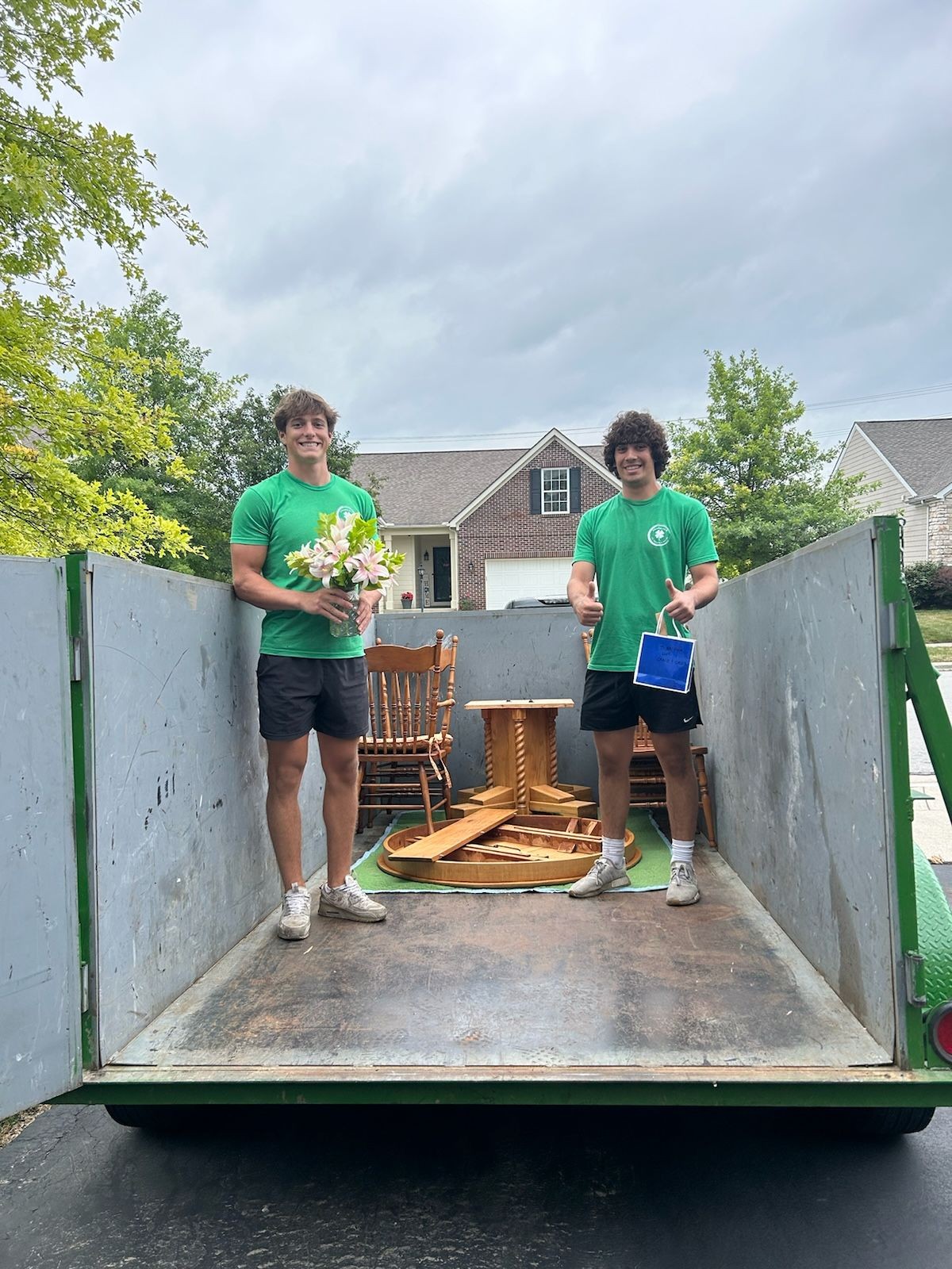 Two Shamrock Junk removal employees standing in a trailer with wooden furniture pieces and a rocking chair.