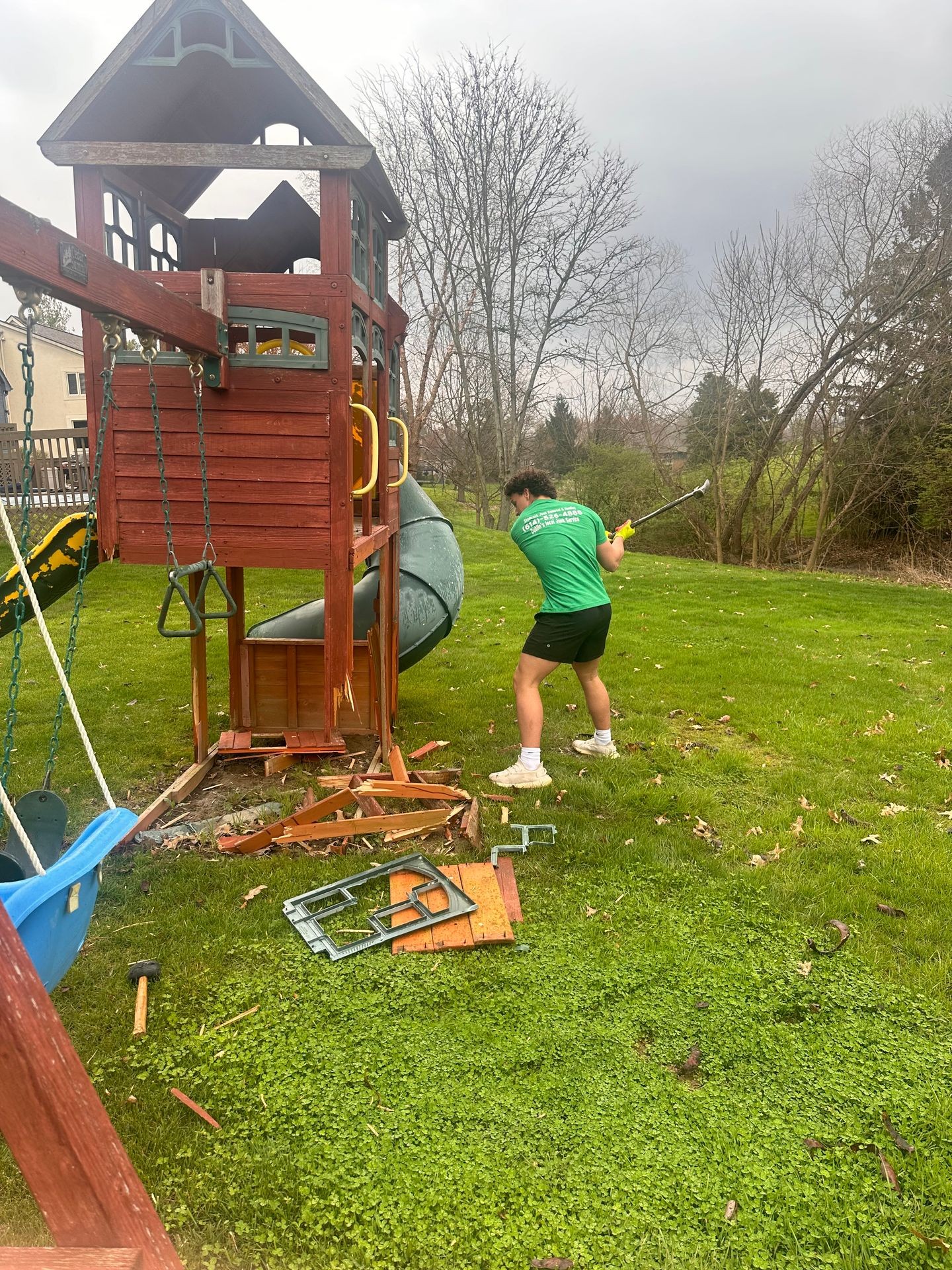 Shamrock Junk Removal employee breaking apart a damaged wooden playset on a grassy backyard.